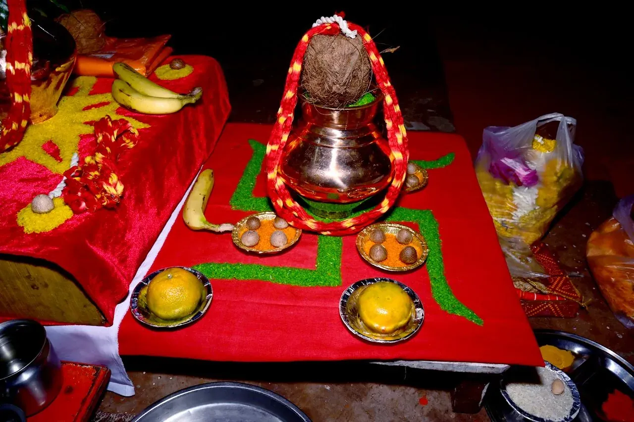 Hindu puja setup with kalash, coconut, banana, sweets, and sacred symbols on red cloth during traditional Indian religious ritual