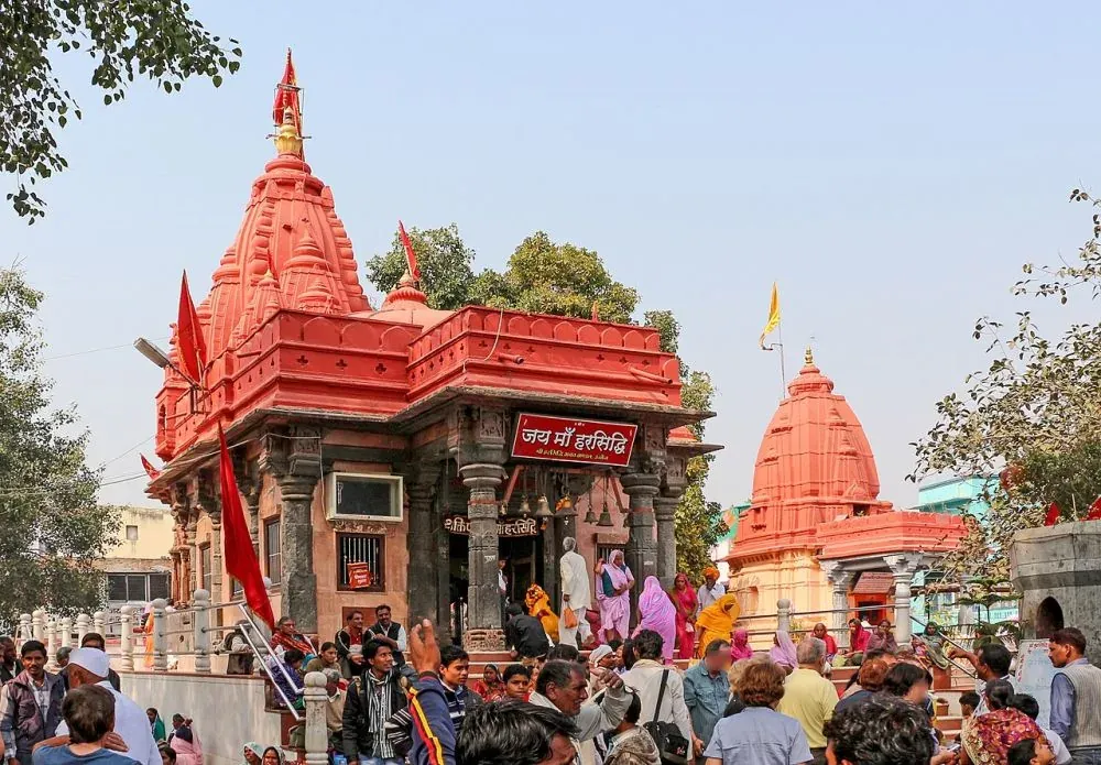 Crowded temple with vibrant red spires and intricate architecture, featuring devotees gathered around the Maa Harsiddhi shrine, showcasing Hindu religious culture and devotion.