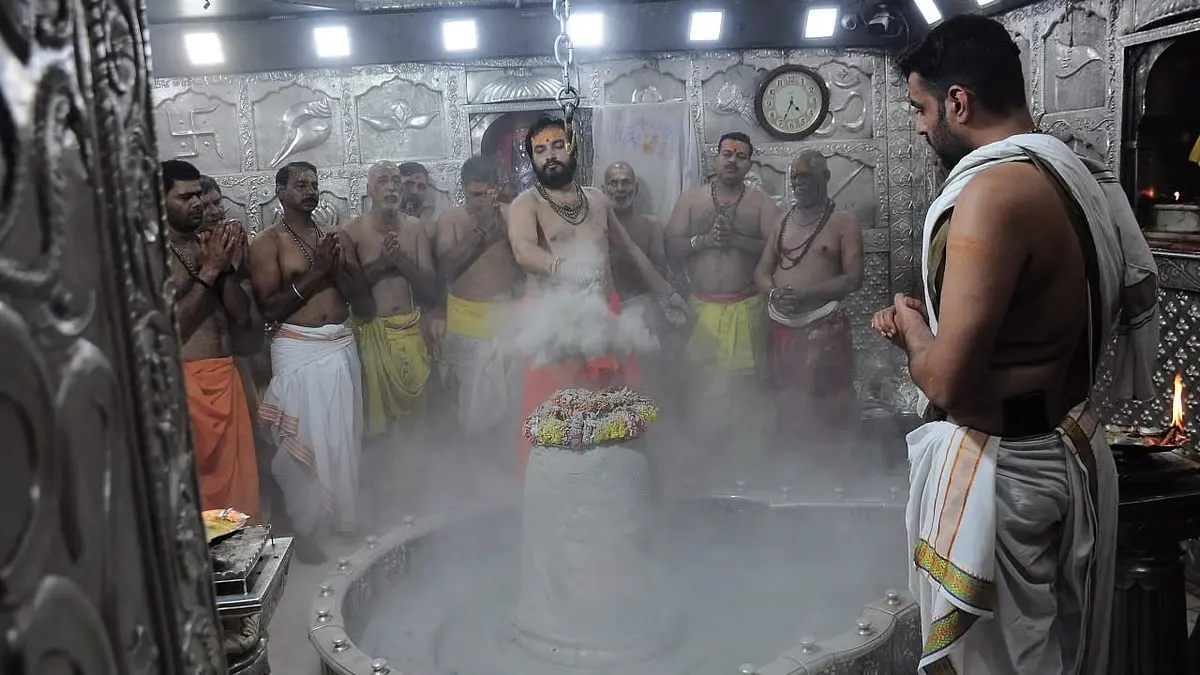 Priests performing Bhasma Aarti at Mahakaleshwar Temple in Ujjain, applying sacred ash to the Shiva Lingam amidst chanting and traditional rituals, surrounded by devotees in dhotis during early morning worship.