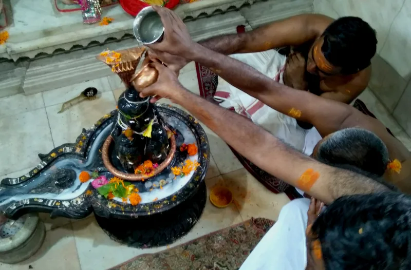 Devotees performing a traditional ritual with a Shiva Lingam, pouring water and offering flowers in a temple setting, showcasing Hindu spirituality and devotion.